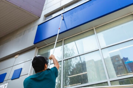 A The Exterior Group technician standing on a ladder to clean upper-story windows.