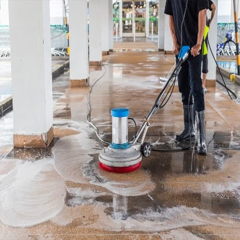 A female The Exterior Group technician using a professional grade pressure washer to clean a stone patio.